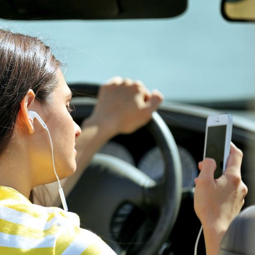 Jeune conductrice au volant qui regarde son téléphone mobile