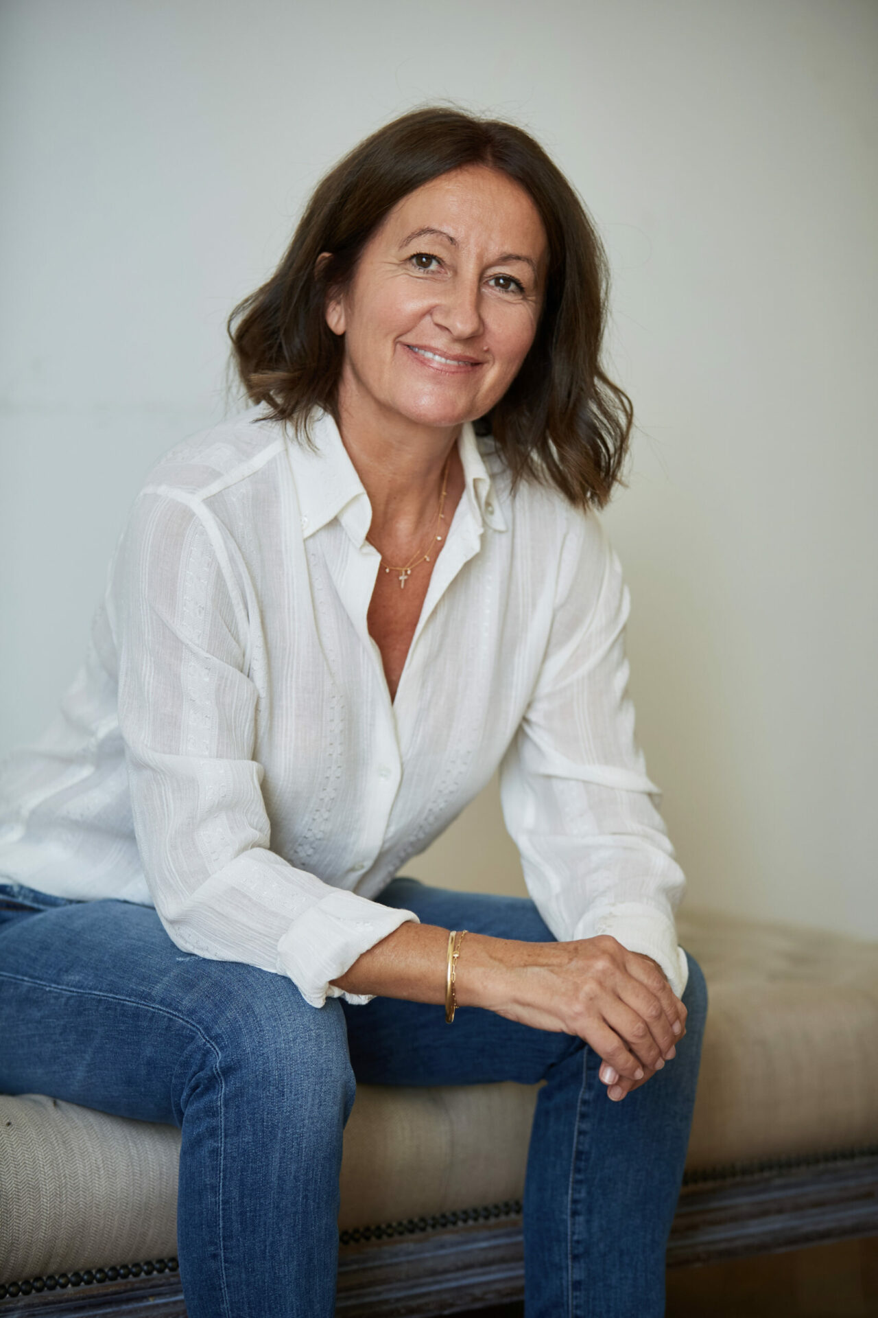 Maître Vanessa Brandone, assise en jean et chemise bleue, souriante, les mains croisées.