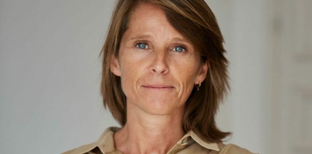 Maître Romy Collard chemise beige bras croisés debout arrière plan blanc gris...