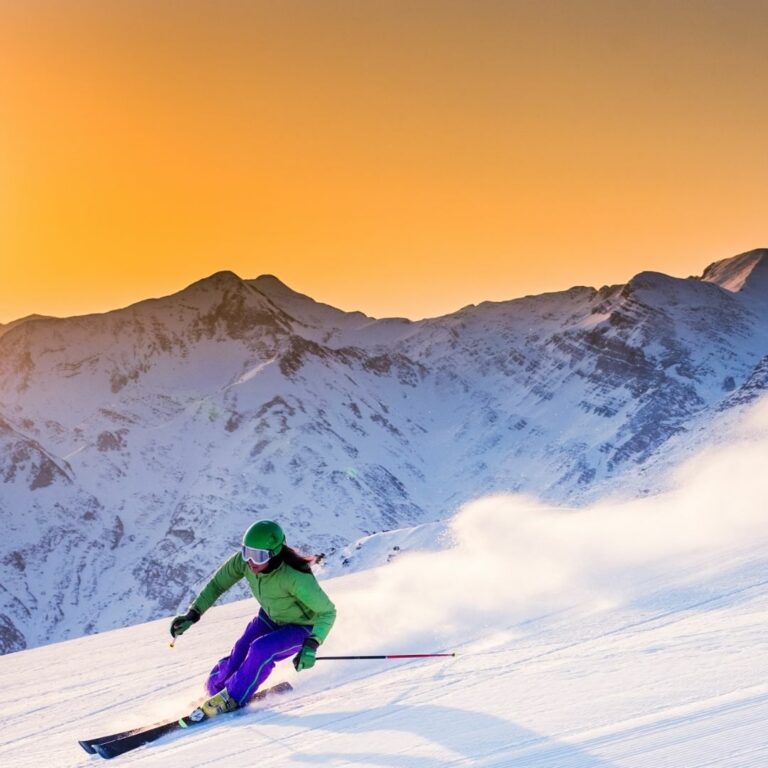 sommet de montagne enneigé ciel orangé, un skieur en monoski dévale la piste sur la neige blanche