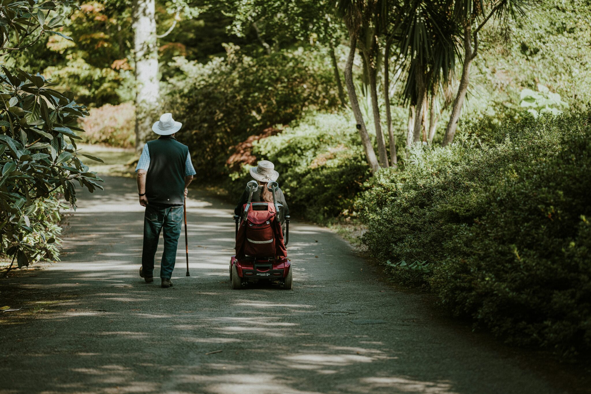 Deux personnes dans un parc, portant des chapeaux, un homme avec une béquille et l'autre personne en fauteuil roulant.