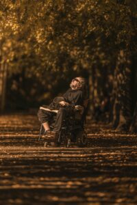 Un homme en fauteuil roulant avec une barbe et des lunettes noires semble prendre le soleil au milieu de la naturee