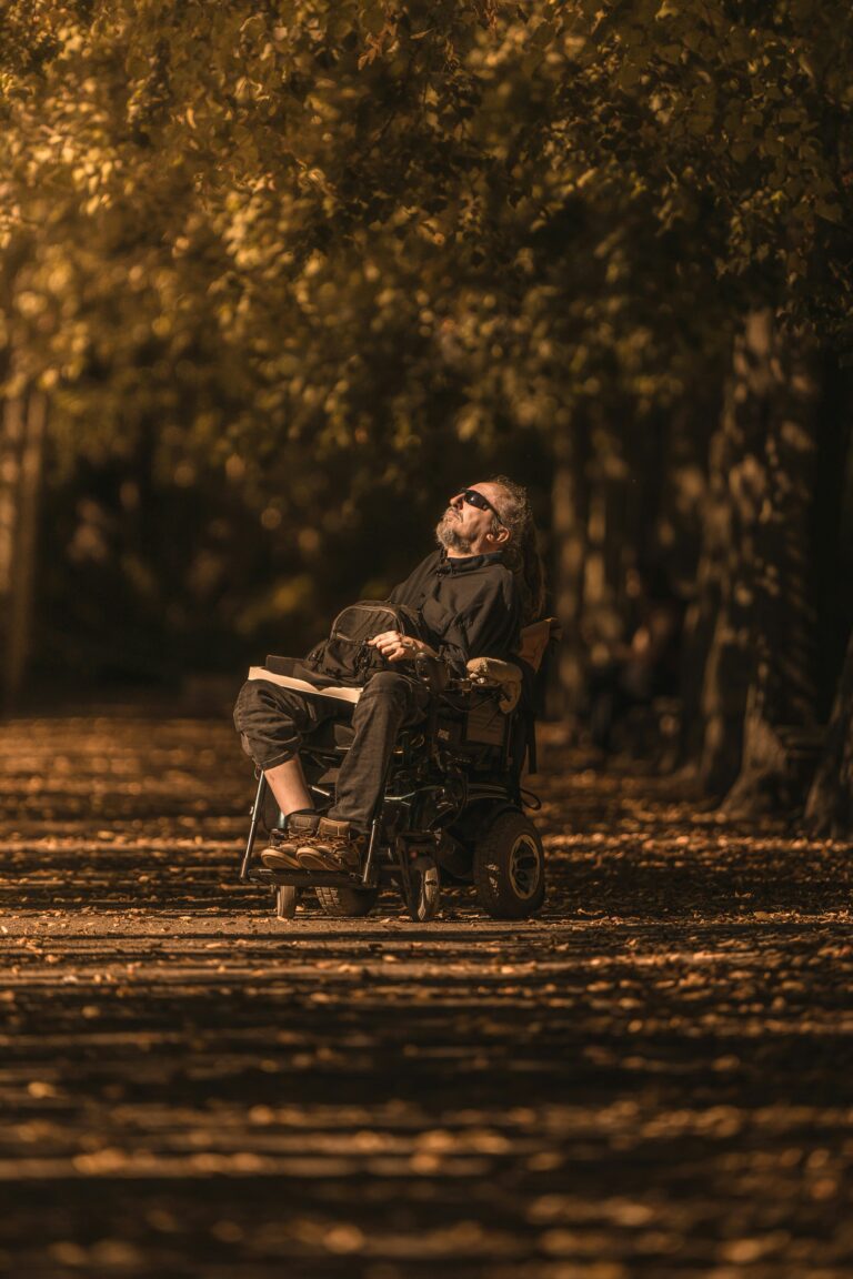 Un homme en fauteuil roulant avec une barbe et des lunettes noires semble prendre le soleil au milieu de la naturee